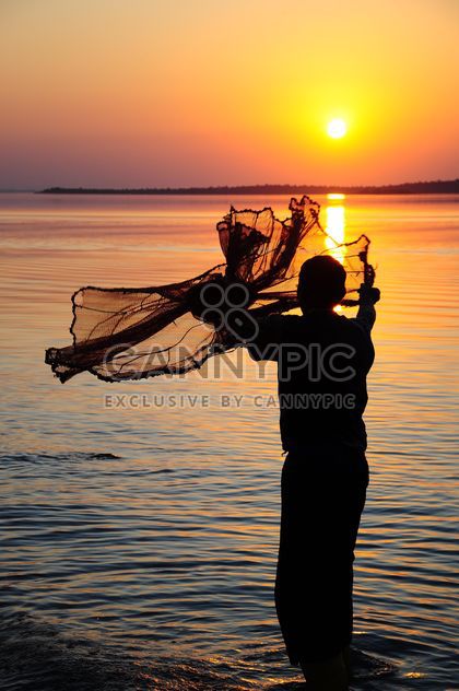 a fisherman throwing net through the sea sunset sun sundown sea man fisherman net dusk people yellow fishin - Free image #185771