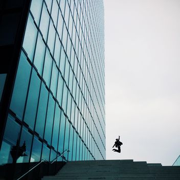 Man jumping by Modern building exterior with glass and metallic facade - image #439121 gratis