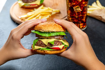 A woman holding a large hamburger on the background of fast food - image #464061 gratis