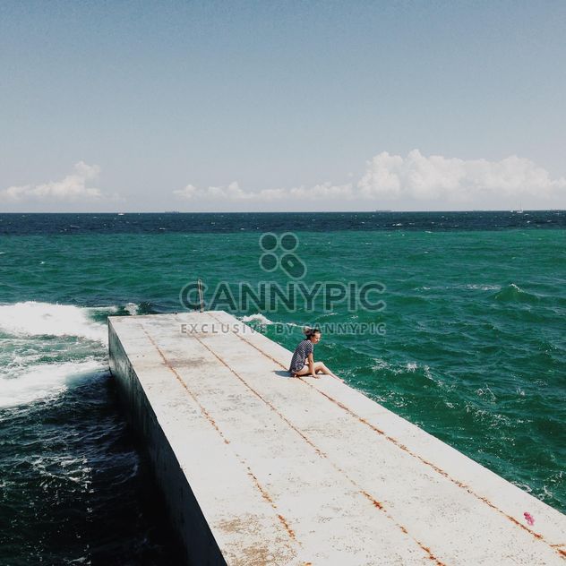girl sitting on a wooden pier near the sea - image #273801 gratis
