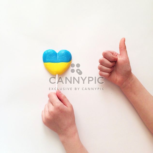 Child's hands and lollipop in colors of Ukrainian flag on white background - Free image #329301
