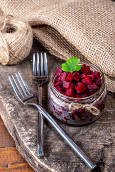 Boiled beet cubes in a glass jar on a wooden background with burlap and forks - бесплатный image #460571
