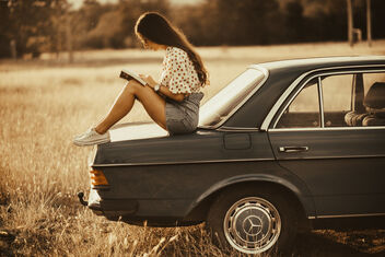 A woman sitting on the trunk of a car and reading the book in nature. Vintage education concept. - Free image #475171